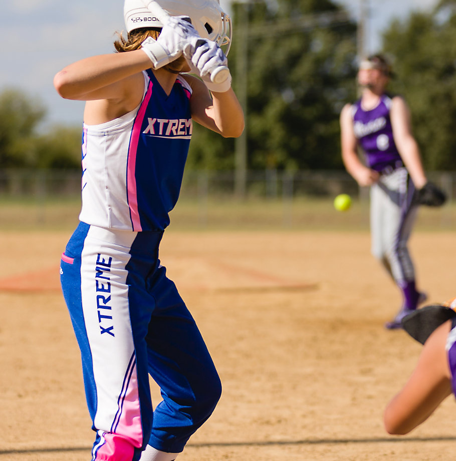 A softball player at bat in a blue, pink and white jersey