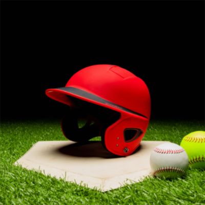 A red batting helmet on a plate next to two baseballs
